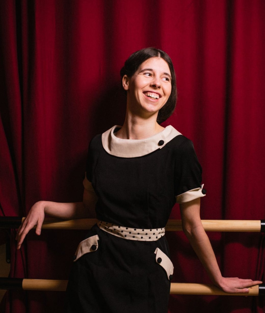 Ruby Doo lächelnd an der Ballettstange vor rotem Vorhang